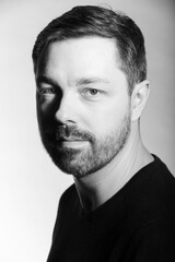 Fototapeta premium Black and white studio portrait of a 40 year old caucasian male. Men's fashion photoshoot. He has a beard and dark hair. 