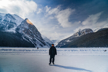 Naklejka na ściany i meble man ice skating on frozen lake luise during winter with mountains on background