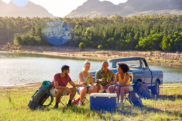 Group Of Friends With Backpacks By Pick Up Truck On Road Trip Drinking Beer From Cooler By Lake