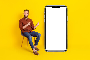 Full length portrait of handsome guy sit chair indicate fingers empty space isolated on yellow color background