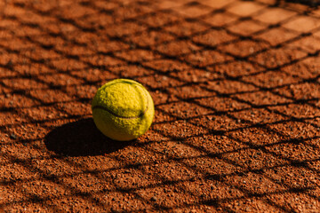 Light orange empty outdoor clay court surface dry grungy ground baseline detail for playing tennis with net shadow in sunny day, yellow green ball, gravel texture background, copy space for text 
 - obrazy, fototapety, plakaty