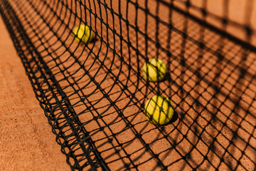 Light orange empty outdoor clay court surface dry grungy ground baseline detail for playing tennis with net shadow in sunny day, yellow green balls, gravel texture background, copy space for text 

 - obrazy, fototapety, plakaty