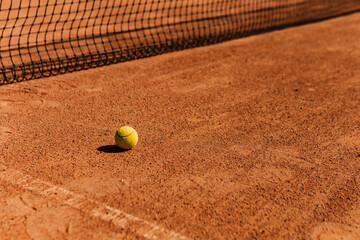 Light orange empty outdoor clay court surface dry grungy ground baseline detail for playing tennis with net in sunny day with yellow green ball, gravel texture background, copy space for text 

 - obrazy, fototapety, plakaty