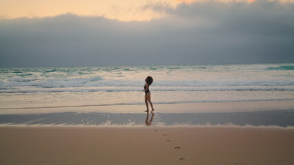 Exotic model posing waves cloudy evening. Woman walking on wet sand near ocean.