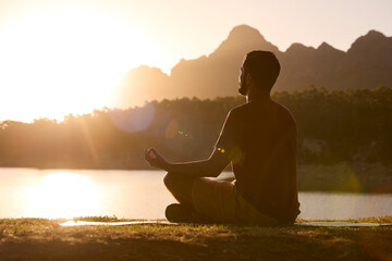 Man Meditating Doing Yoga By Lake And Mountains At Sunset