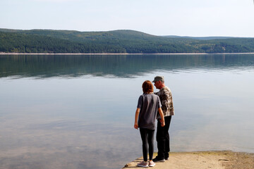 a teenage girl with her father are standing on the shore of a beautiful forest lake
