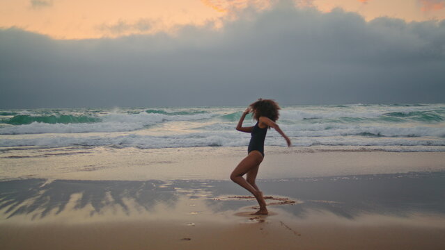 Girl dancing wet sand near ocean waves cloudy evening. Woman performing dance.