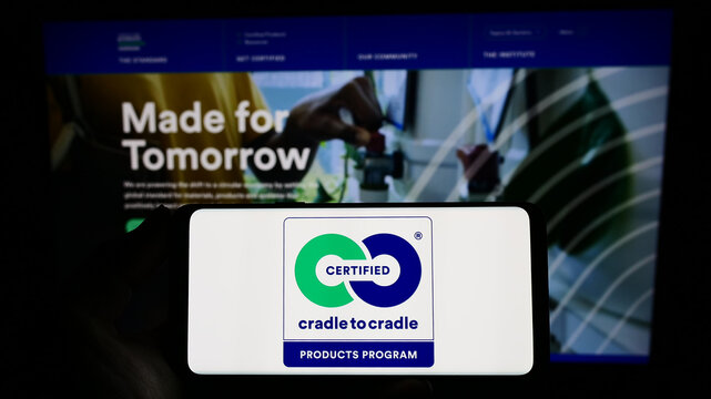Stuttgart, Germany - 03-11-2023: Person holding smartphone with logo of environmental label Cradle to Cradle Certified on screen in front of website. Focus on phone display.