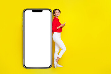 Photo of lovely positive girl with bob hairstyle wear red shirt hold phone demonstrating touchscreen isolated on yellow color background