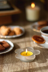 Scented candles, chocolate, cookies, cup of tea, books, e-reader, glasses and flowers on the table. Hygge at home. Selective focus.
