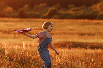 The girl runs across the summer field and launches a toy plane into the sky. A child plays aviator...