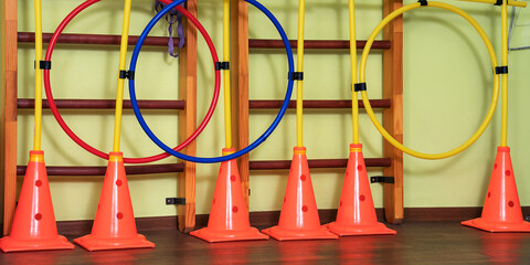 Bright orange colored sport cones stands on gymnasium floor. Training and practice workout concept. Sport outfit and equipment.