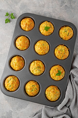 Homemade zucchini muffins with cheese, garlic and herbs in a baking form on a gray concrete background. Vegetarian dish. Copy space, top view.