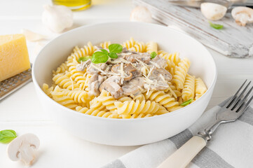 Fusilli pasta with mushrooms, cheese and fresh basil in a plate on a white wooden background.
