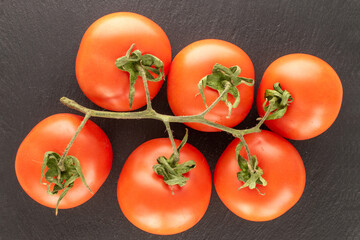 Several ripe tomatoes on a branch on a slate stone, macro, top view.