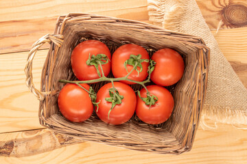 Several fresh tomatoes on a branch in a basket on a wooden table, macro, top view.