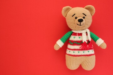 Crochet amigurumi handmade stuffed soft teddy bear toy in colored sweater on red background. Handwork, hobby. Craft diy newborn pregnancy concept. Knitted doll for little baby. Closeup flat lay out