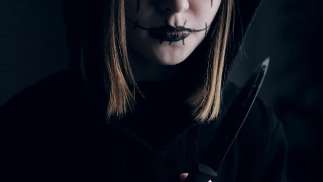 Spooky preteen girl holding knife and looking at camera. Scary child kid in black and Halloween dark makeup with blade weapon