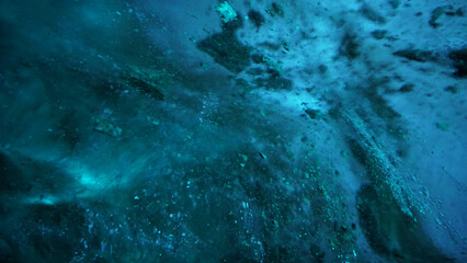 Fototapeta na wymiar Turquoise pure color of ice inside the ice cave. Stones and icicles are visible in places. Light grains of snow on the ice walls. Frozen air bubbles in an ice wall. An ancient glacier. Color gradient