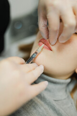 The cosmetologist makes an injection in the lips of a girl for an increase in the cosmetology office with a syringe close-up face