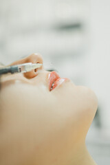 The cosmetologist makes an injection in the lips of a girl for an increase in the cosmetology...