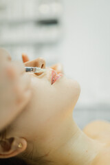 The cosmetologist makes an injection in the lips of a girl for an increase in the cosmetology...