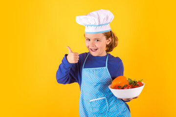 Kid cook hold plate with vegetables. Chef kid preparing healthy food. Portrait of child with chef hats.