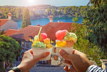 Couple with beautiful bright sweet ice cream of different flavors in the hand.Background of   view of the see and old street  in  Rovinj , Croatia. Traveling concept background - 581558387
