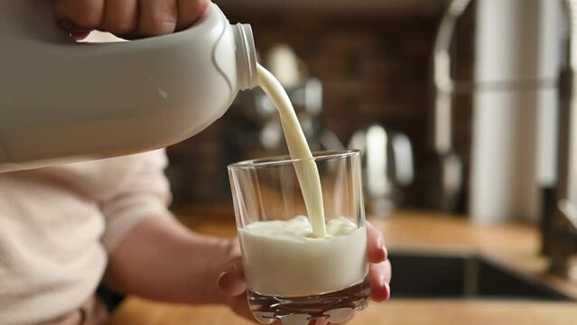Girl with pouring milk in glass at kitchen at home