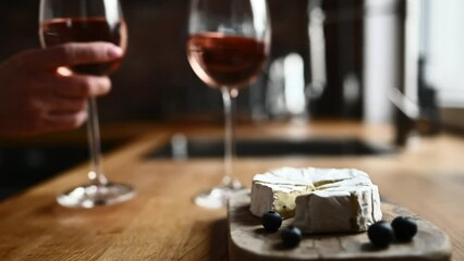 Cheese brie and man put glasses with rose wine on table at kitchen. Elegant creamy camembert food and alcohol grape drink