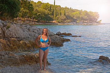 A woman on a rocky beach in Croatia.Amazing sunny day in the summer, green forest in the background - 581559775