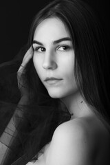 Fashion portrait of a beautiful caucasian model in her 20s. She is wrapped in tulle fabric. The background is black and she is posing. The model has brown eyes and long hair.