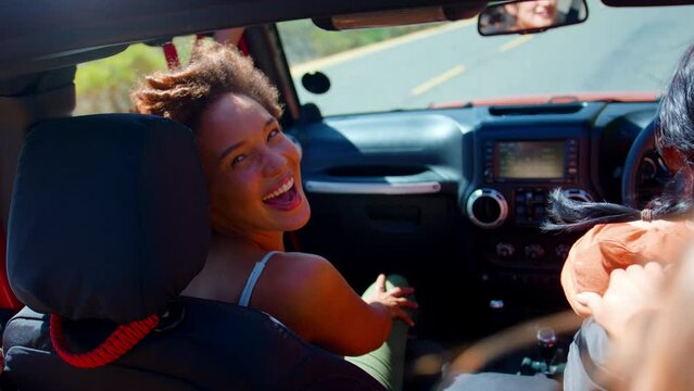 Portrait of female friends in open top car laughing on road trip through countryside - shot in slow motion
