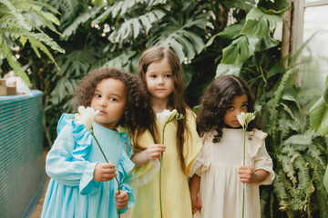Three little girls in the garden with flowers in their hands. children of different nationalities.
