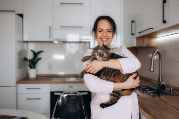 Young woman playing with cat in kitchen at home.