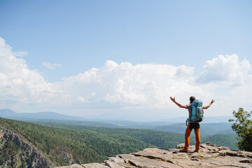 A man triumphantly threw his hands up standing on the top of the mountain, trekking alone in the...