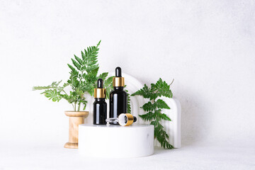 Set of natural organic skin care serums in glass bottles with dropper on white marble background with clay geometric decorations and fern leaves close up. Skin care concept.
