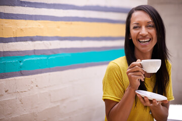 Shes got some big ideas. an attractive woman drinking tea with a colorful wall behind her.