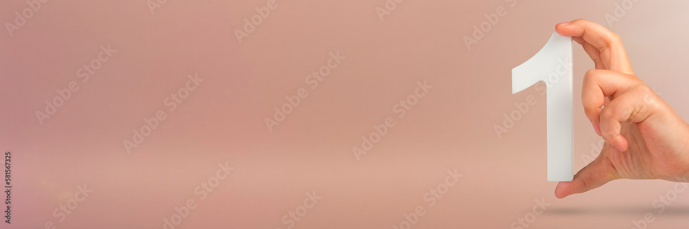 Aufkleber Number one in hand. A hand holds a white number one on a red background with copy space. Concept with number one. 1 percent rate, birthday, first or winner.