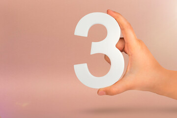 Number three in hand. Hand holding white number 3 on red background with copy space. Concept with...