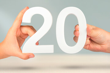 Number twenty in hand. Hand holding white number 20 on blurred background with copy space. Concept...