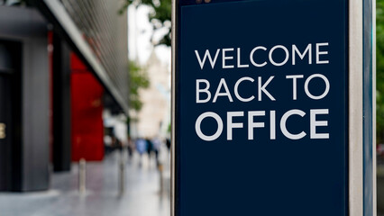Welcome back to the office on a city-center sign in front of a modern office building	
