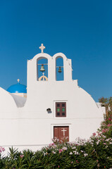 Facade of a white-walled Orthodox church with a bellflower against the blue sky on the island of Santorini in Greece