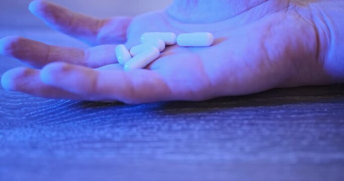 Immobile hand with handful of pills lies on floor. Red-blue flashing light on background. Concept of death from an overdose of pills, painkillers, antidepressants. Close-up.