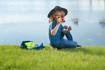 Child with binoculars travelling outdoors. Boy traveler with backpack in a summer day. Portrait of a little boy exploring wildlife. Hiking and adventure concept.