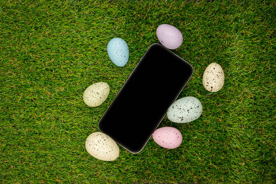 Phone with blank empty screen on background of easter eggs with  in  on green grass. Space for text. Happy Easter! Smartphone mockup, top view