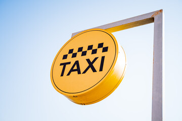 A taxi sign hangs against the sky, a taxi stop, a yellow banner with black text, letters in a...