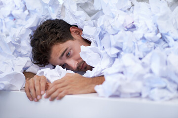 Hes almost given up. a businessman buried under a pile of crumpled up paperwork.