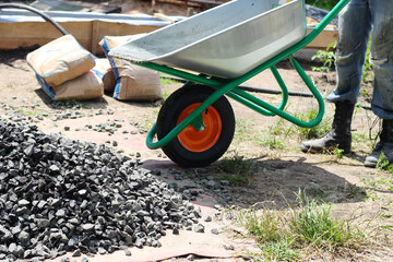 The worker is pouring out crushed stones on the ground from wheelbarrow, as part of a building...