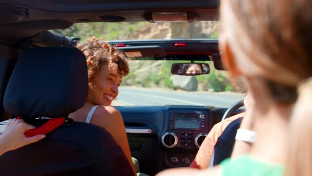 Group of female friends in open top car laughing on road trip through countryside - shot in slow motion